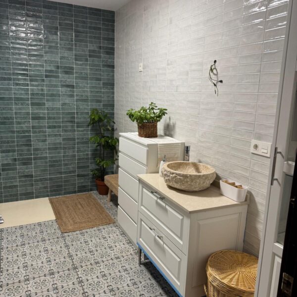 Cuarto de baño reformado con alicatado blanco, pared en tonos verdes y plato de ducha moderno.