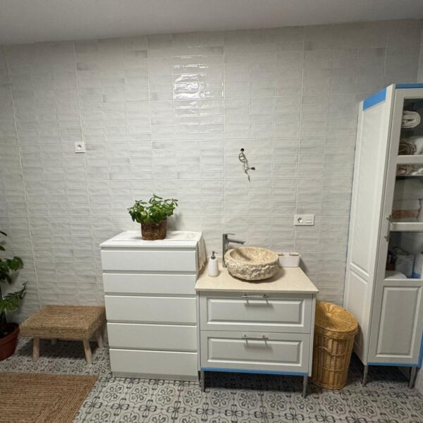 Cuarto de baño reformado con alicatado blanco, pared en tonos verdes y plato de ducha moderno.