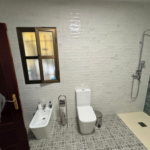Cuarto de baño reformado con alicatado blanco, pared en tonos verdes y plato de ducha moderno.