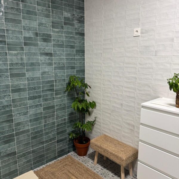 Cuarto de baño reformado con alicatado blanco, pared en tonos verdes y plato de ducha moderno.