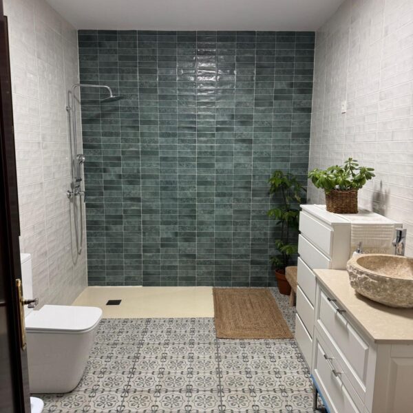 Cuarto de baño reformado con alicatado blanco, pared en tonos verdes y plato de ducha moderno.