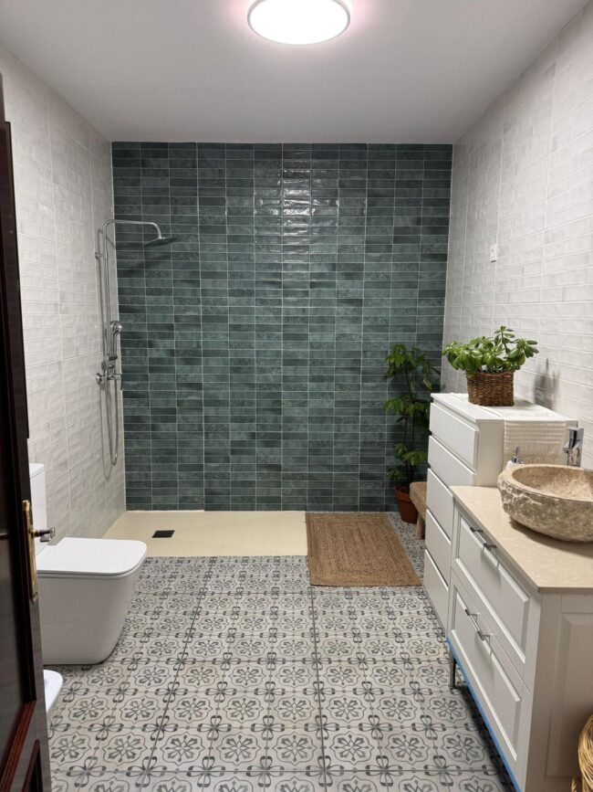 Cuarto de baño reformado con alicatado blanco, pared en tonos verdes y plato de ducha moderno.
